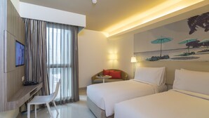 A hotel room with two beds, a desk with a chair, a TV, and a painting of umbrellas. - Travelodge Pattaya (Pattaya)