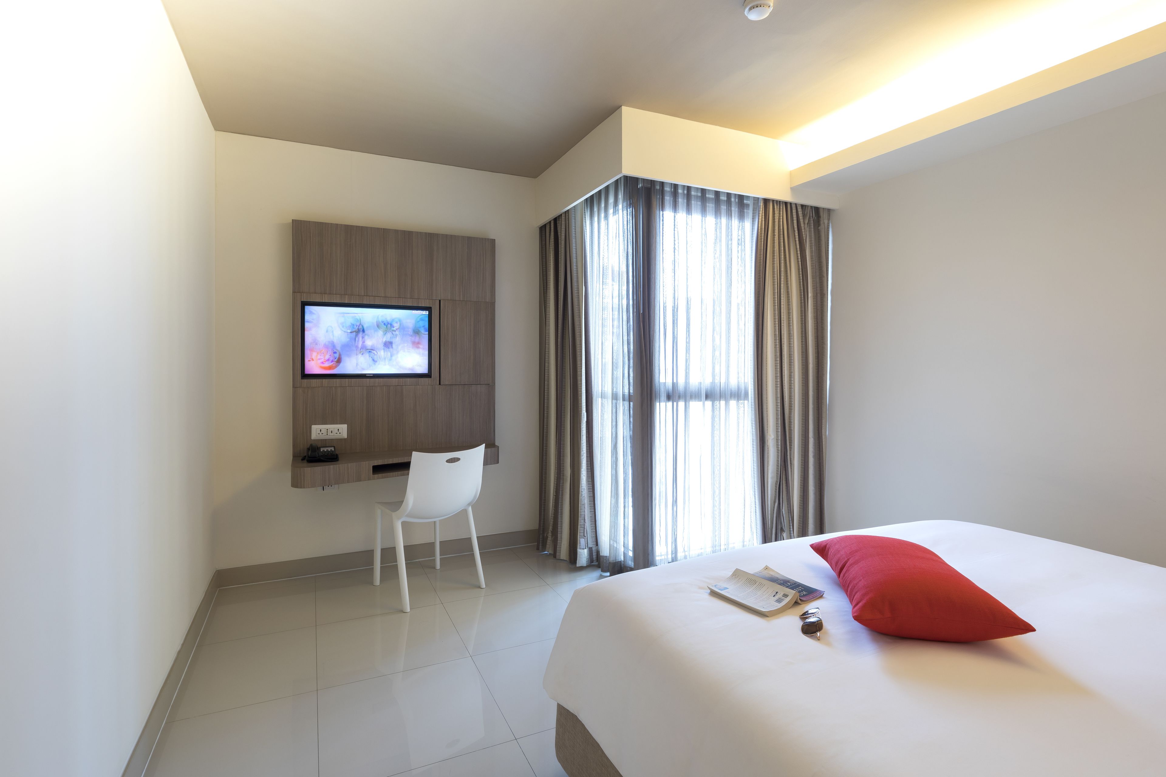 Una camera d'albergo moderna con un letto, una scrivania, una sedia, una TV e una finestra con tende.