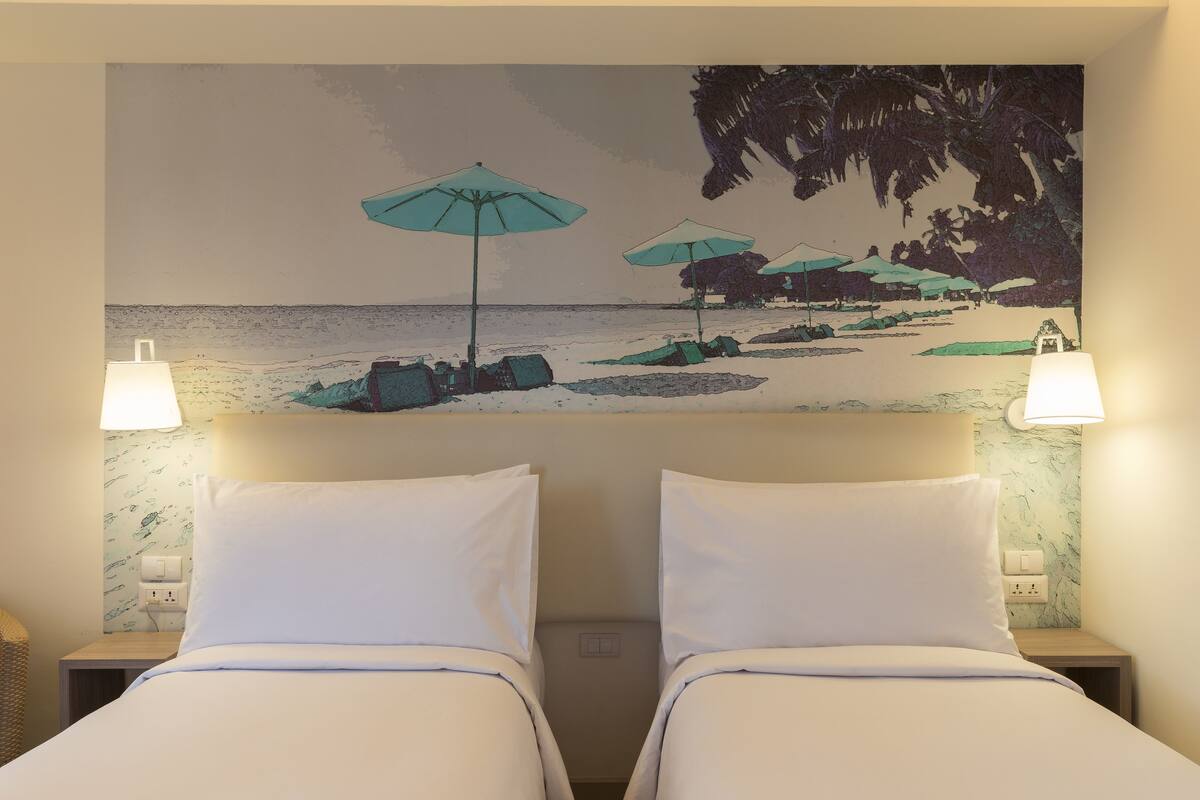 Une chambre d’hôtel avec deux lits, une fresque murale sur le thème de la plage et deux lampes de chevet.