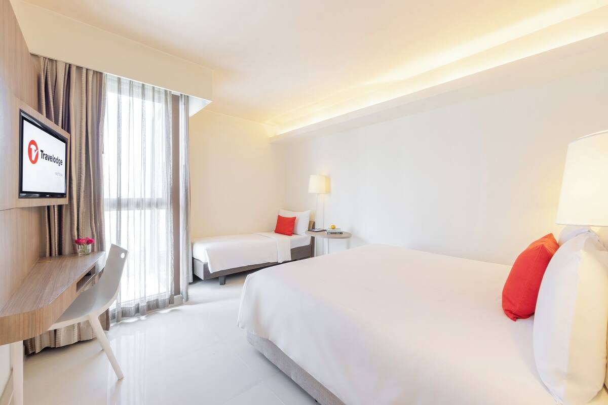 Une chambre d’hôtel équipée d’un bureau, de deux lits, d’une télévision et d’une lampe.