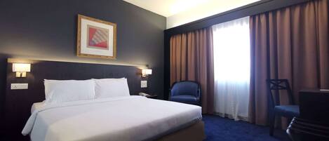 Una habitación de hotel con una cama grande, un escritorio, una silla y un cuadro en la pared.