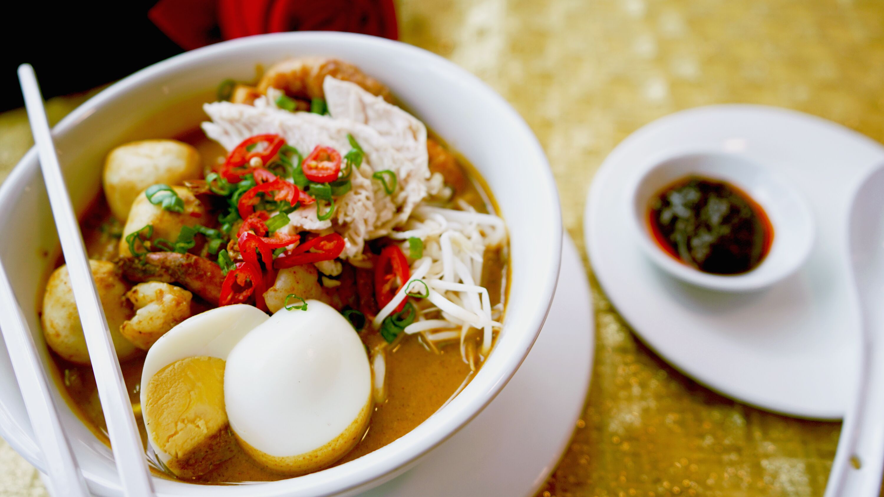 A bowl of soup with noodles, chicken, boiled eggs, and vegetables.