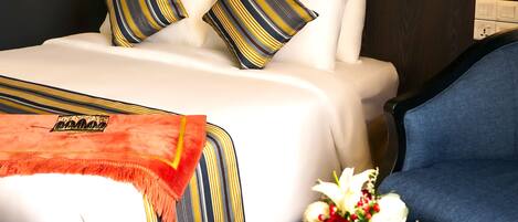 A hotel room with a bed, a blue armchair, a small round table with a vase of flowers, and wall-mounted lamps.