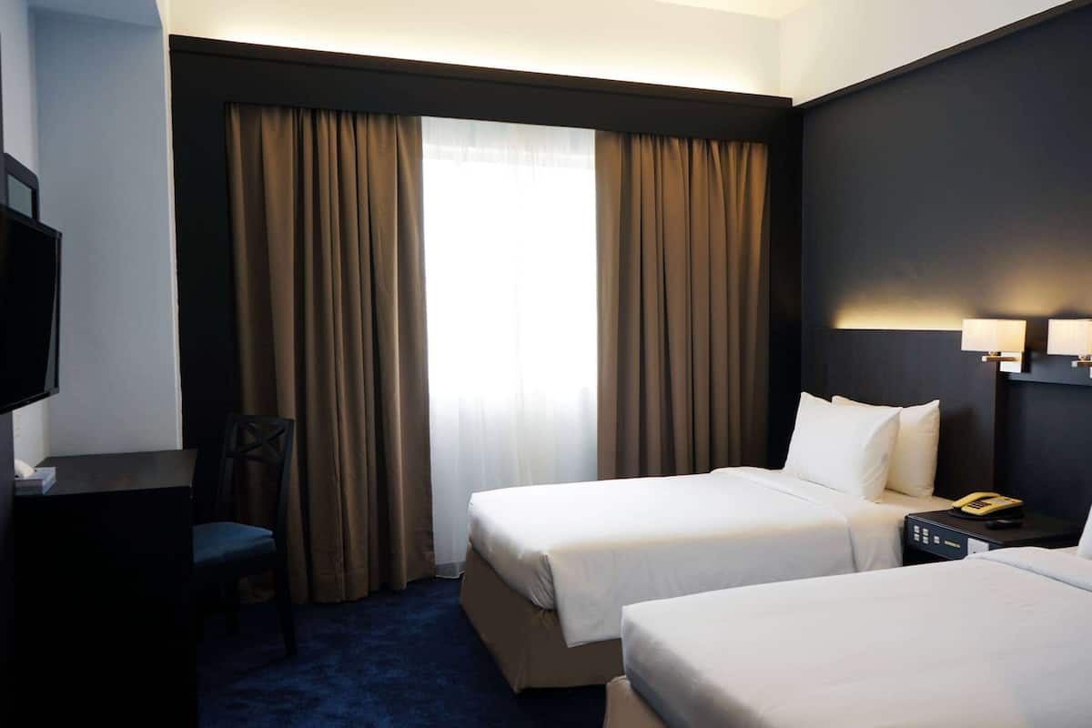 Ein Hotelzimmer mit zwei Betten, einem Schreibtisch, einem Sessel und einem Fernseher.