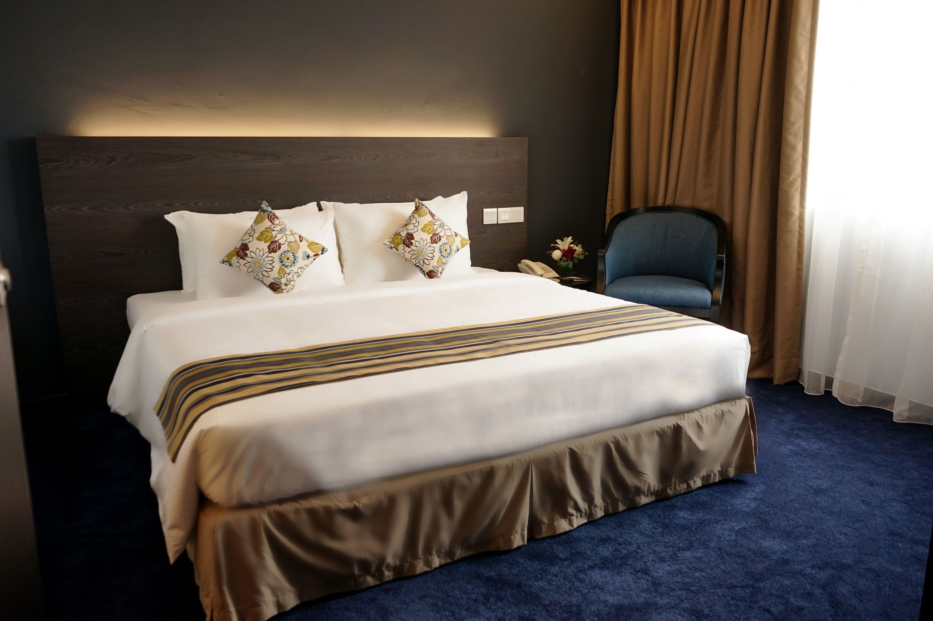A hotel room with a large bed, a headboard, a chair, and a nightstand with a phone.