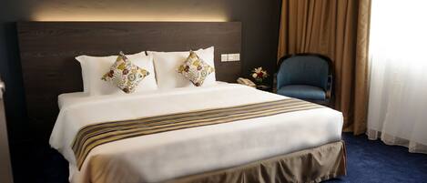 A hotel room with a large bed, a headboard, a chair, and a nightstand with a phone.