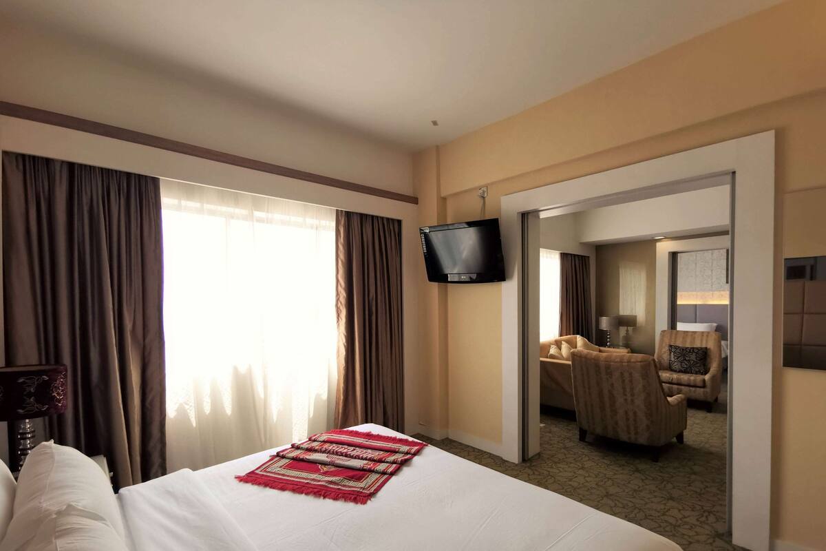 Ein Hotelzimmer mit einem Bett, einem an der Wand befestigten Fernseher und Blick in das angrenzende Zimmer durch eine offene Tür.