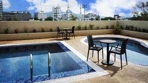 A rooftop pool area with two pools, outdoor seating, and a view of a mosque and cityscape. - Shahzan Hotel Kuantan, Trademark Collection by Wyndham (Kuantan)