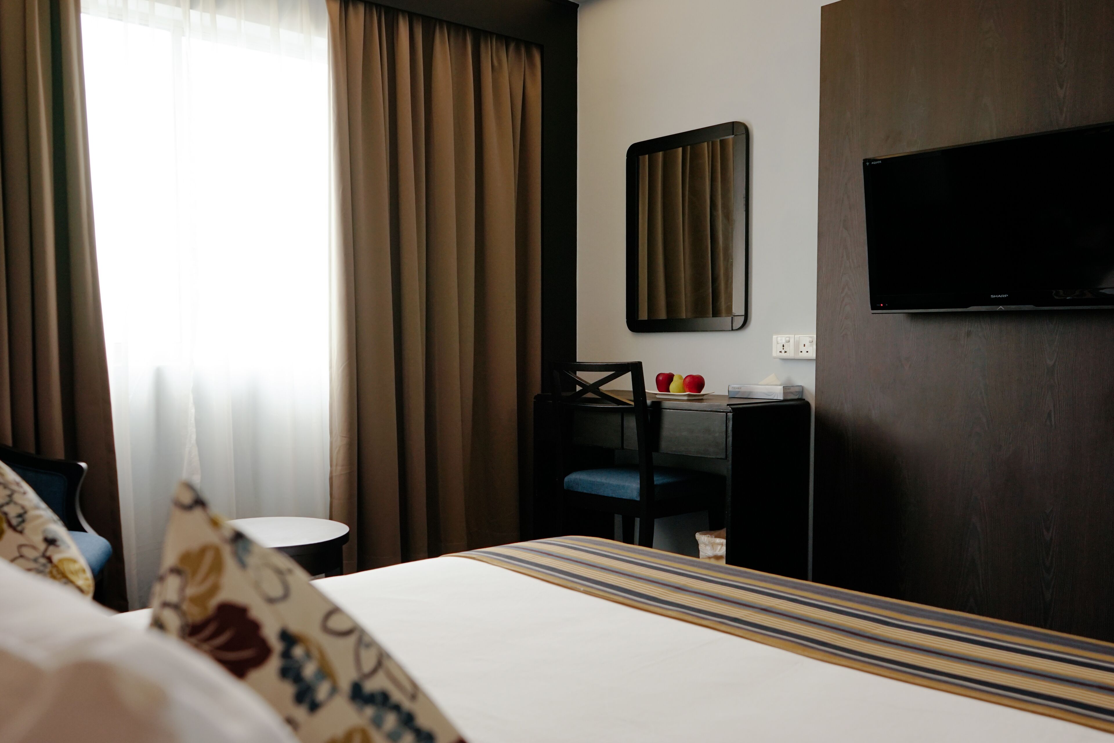 A hotel room with a bed, a desk, a chair, a television, and a window with curtains.