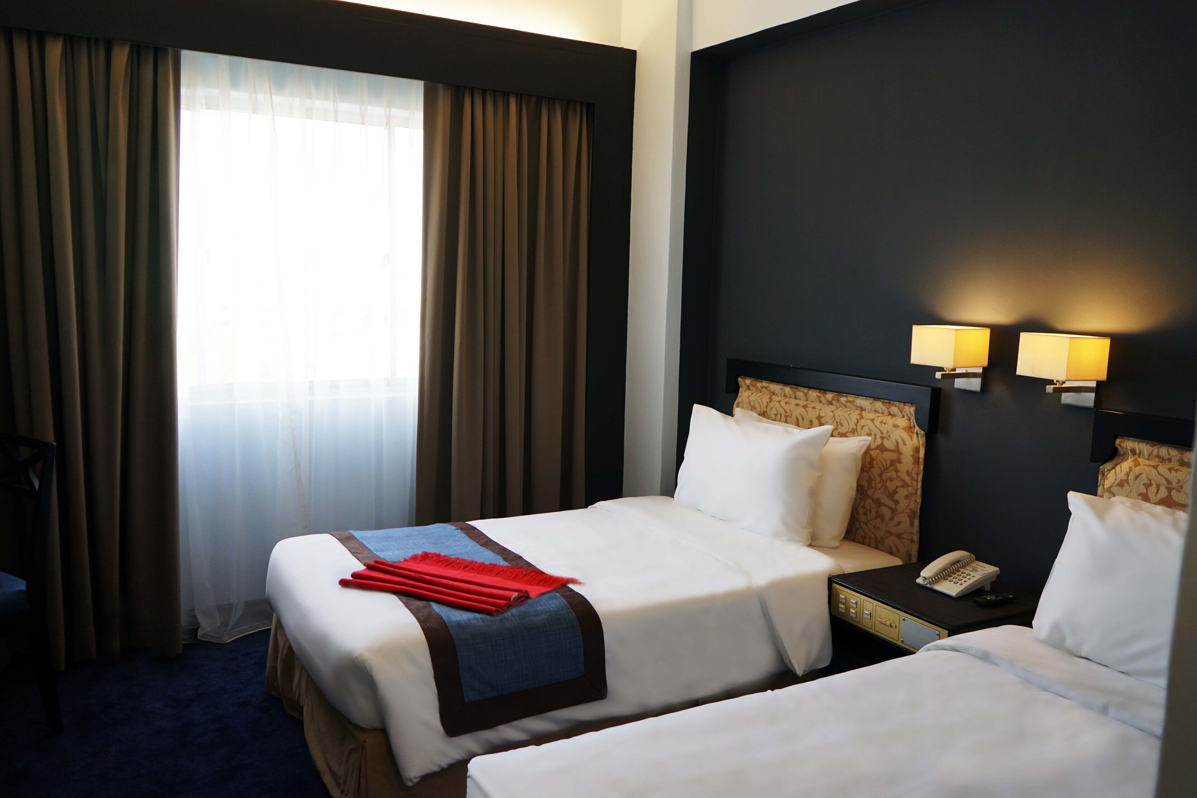 A hotel room with two beds, a nightstand with a phone, and a window with curtains.
