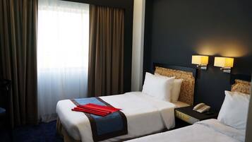 A hotel room with two beds, a nightstand with a phone, and a window with curtains.