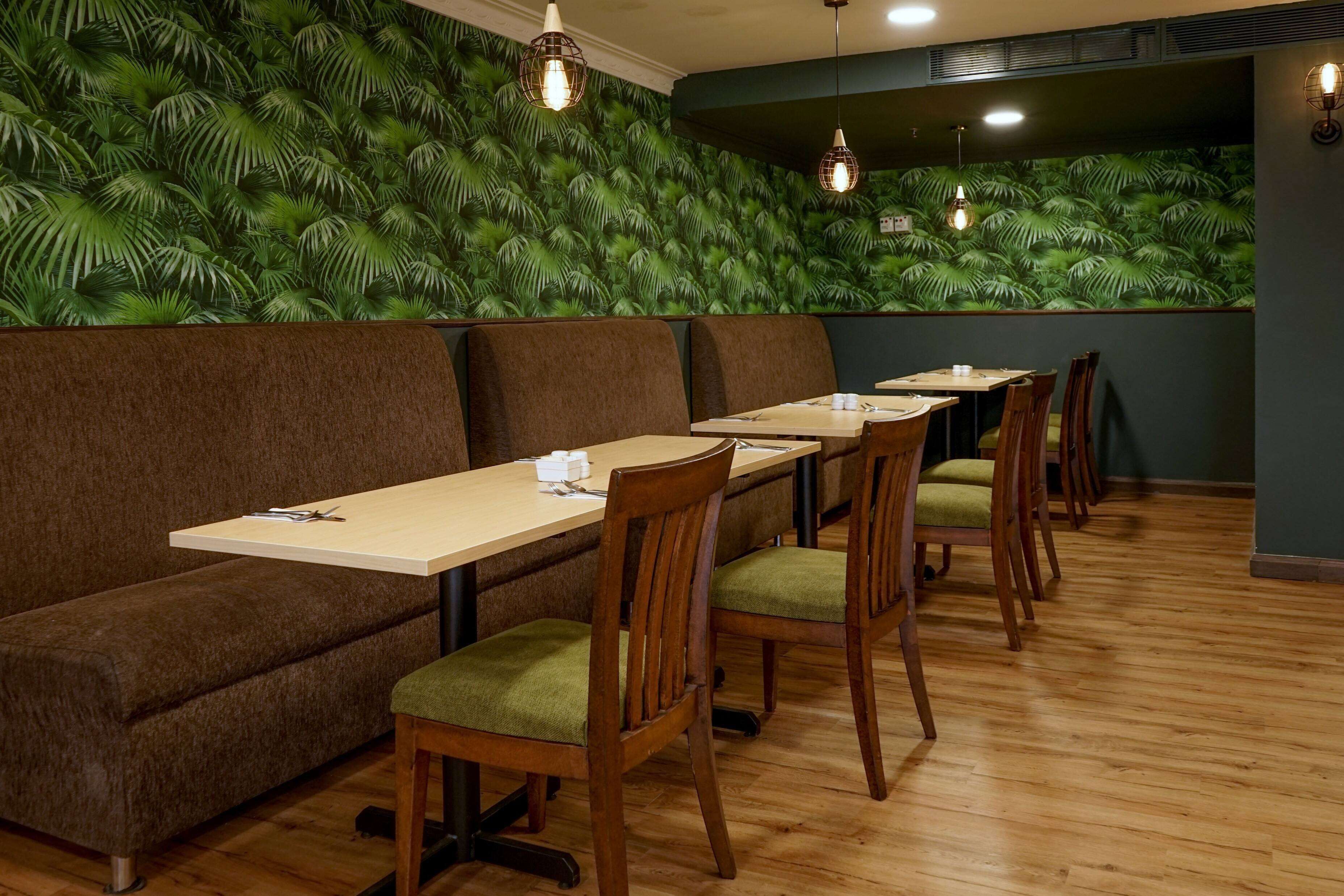 Un restaurante con mesas y sillas de madera, un banco tapizado de color marrón y una pared cubierta de hojas verdes.