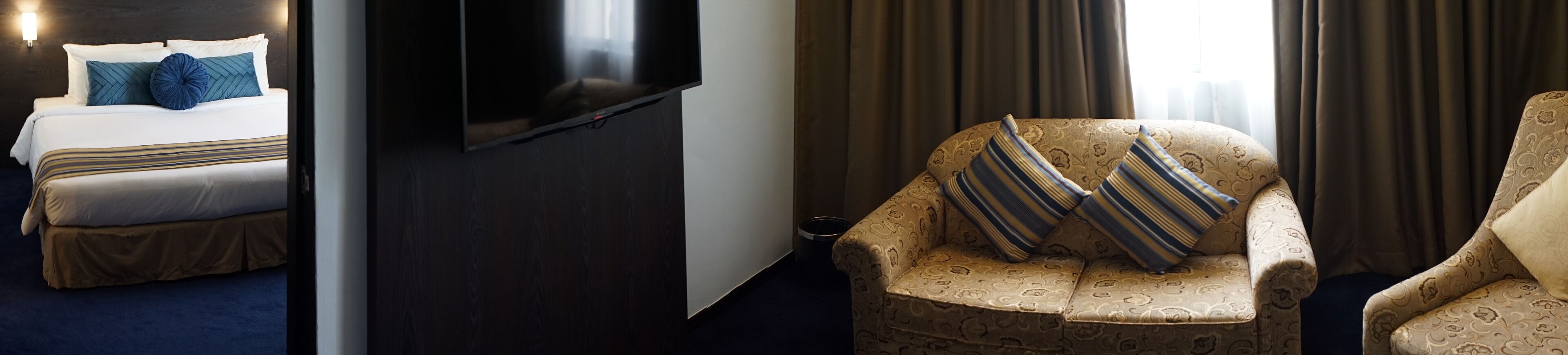 A hotel room with a bed, a television, a sofa, and a patterned armchair.