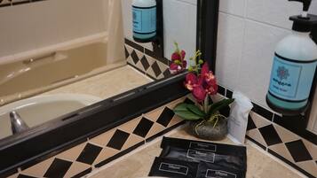 A bathroom with a bathtub, a sink, a mirror, a potted orchid, and toiletries.