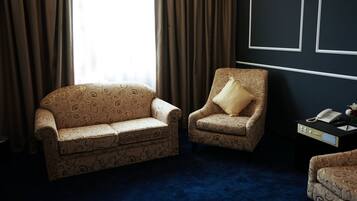 Una habitación con un sofá estampado, un sillón a juego, una pequeña mesa con un teléfono y una alfombra azul oscuro.