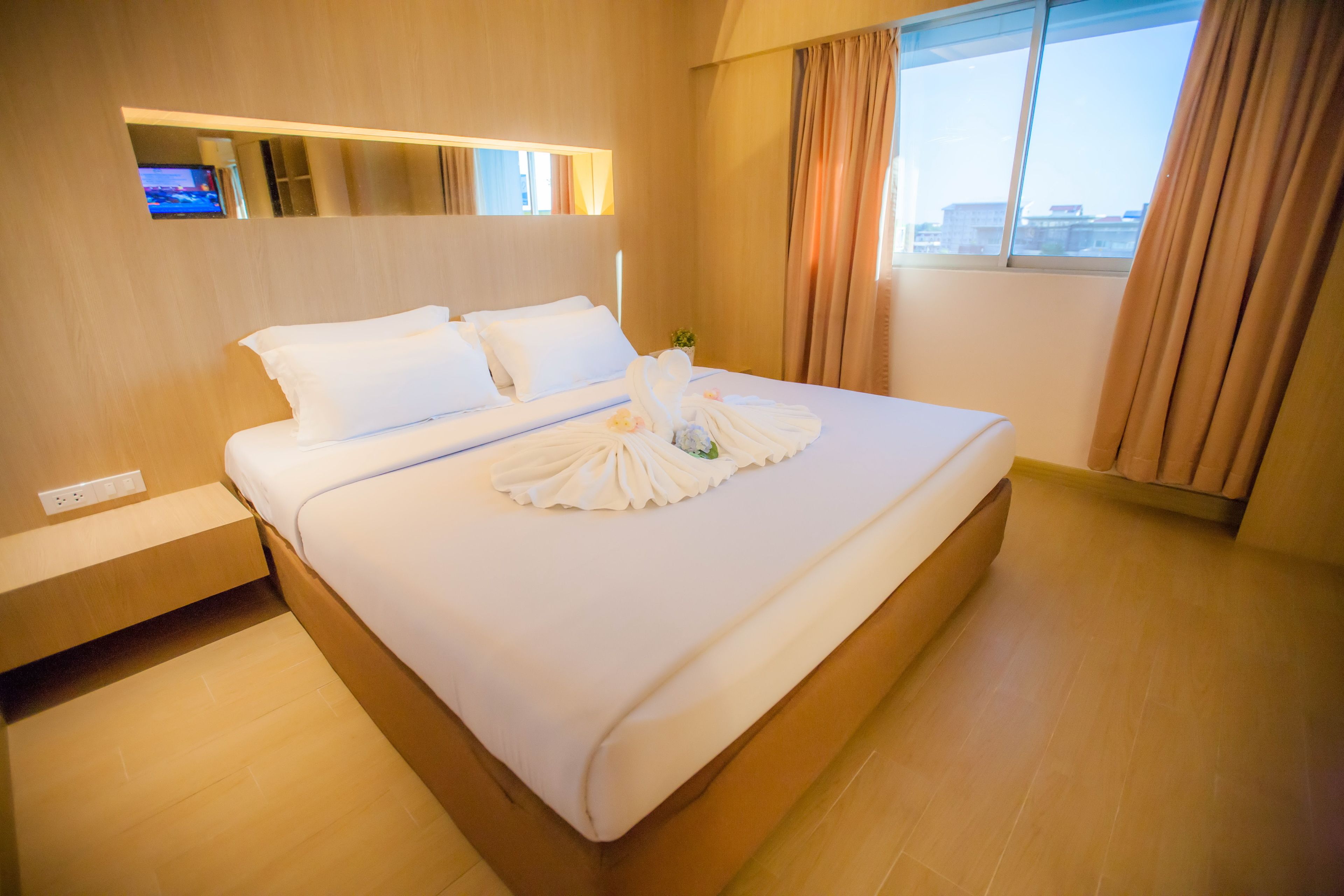 A hotel room with a large bed, a TV mounted on the wall, and a window with curtains.
