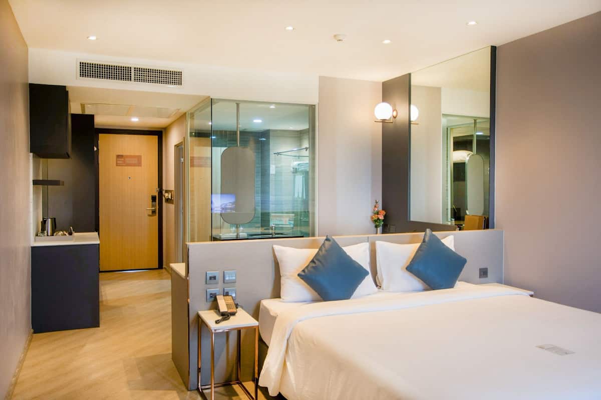 A modern hotel room with a large bed, bedside table, and a mirror.