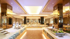 Um hall de hotel moderno com uma recepção central, paredes espelhadas e diversos utensílios de refeição expostos em balcões.