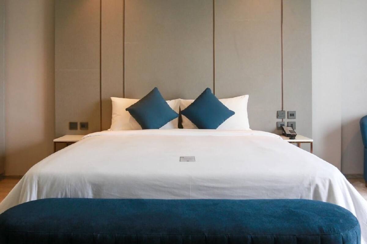A hotel room with a large bed, two pillows, a bedside table with a lamp, and a nightstand.