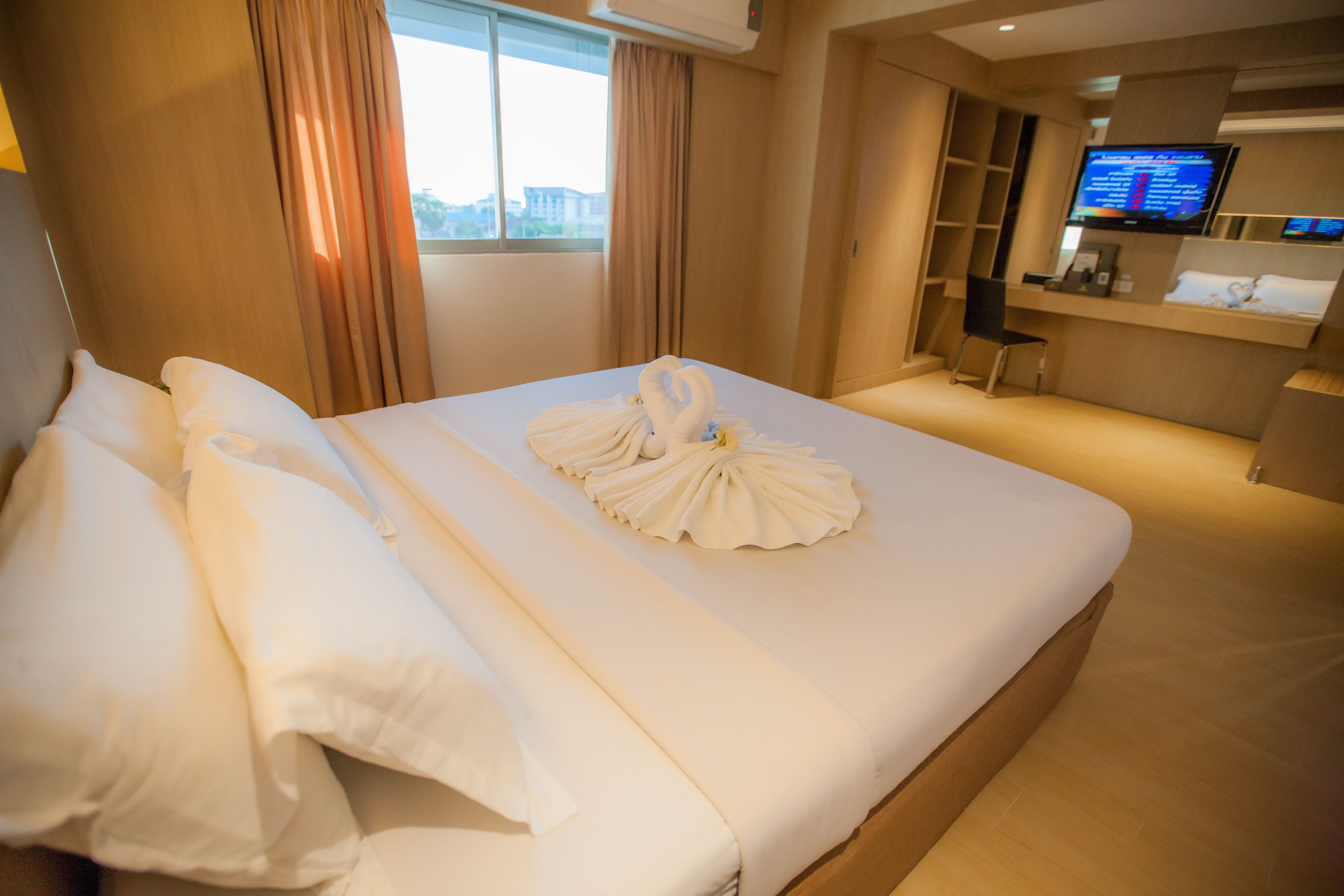 A hotel room with a neatly made bed, a desk with a computer, and a television on the wall.
