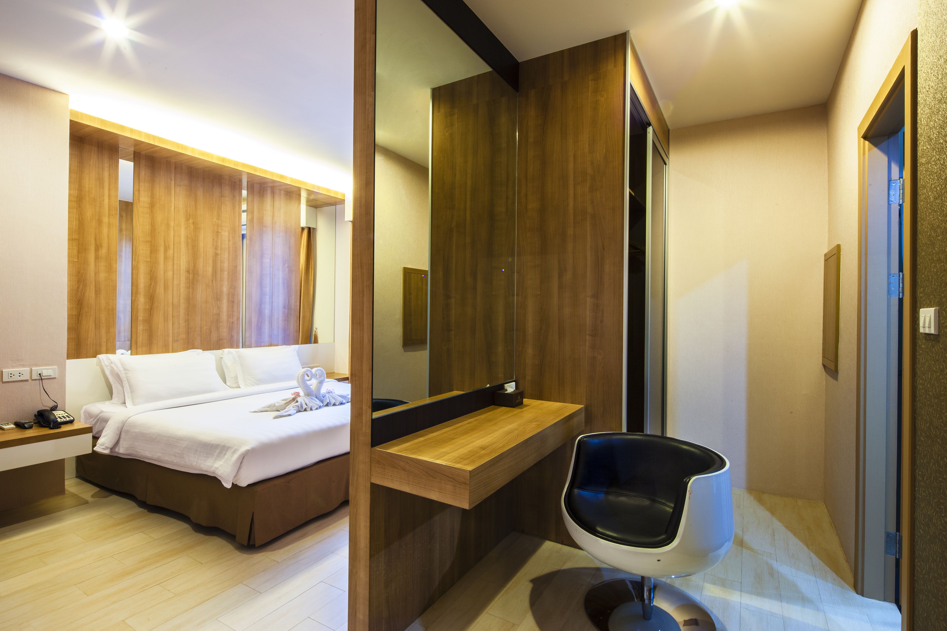 Una habitación de hotel moderna con una cama y tocador de madera, y una silla negra.