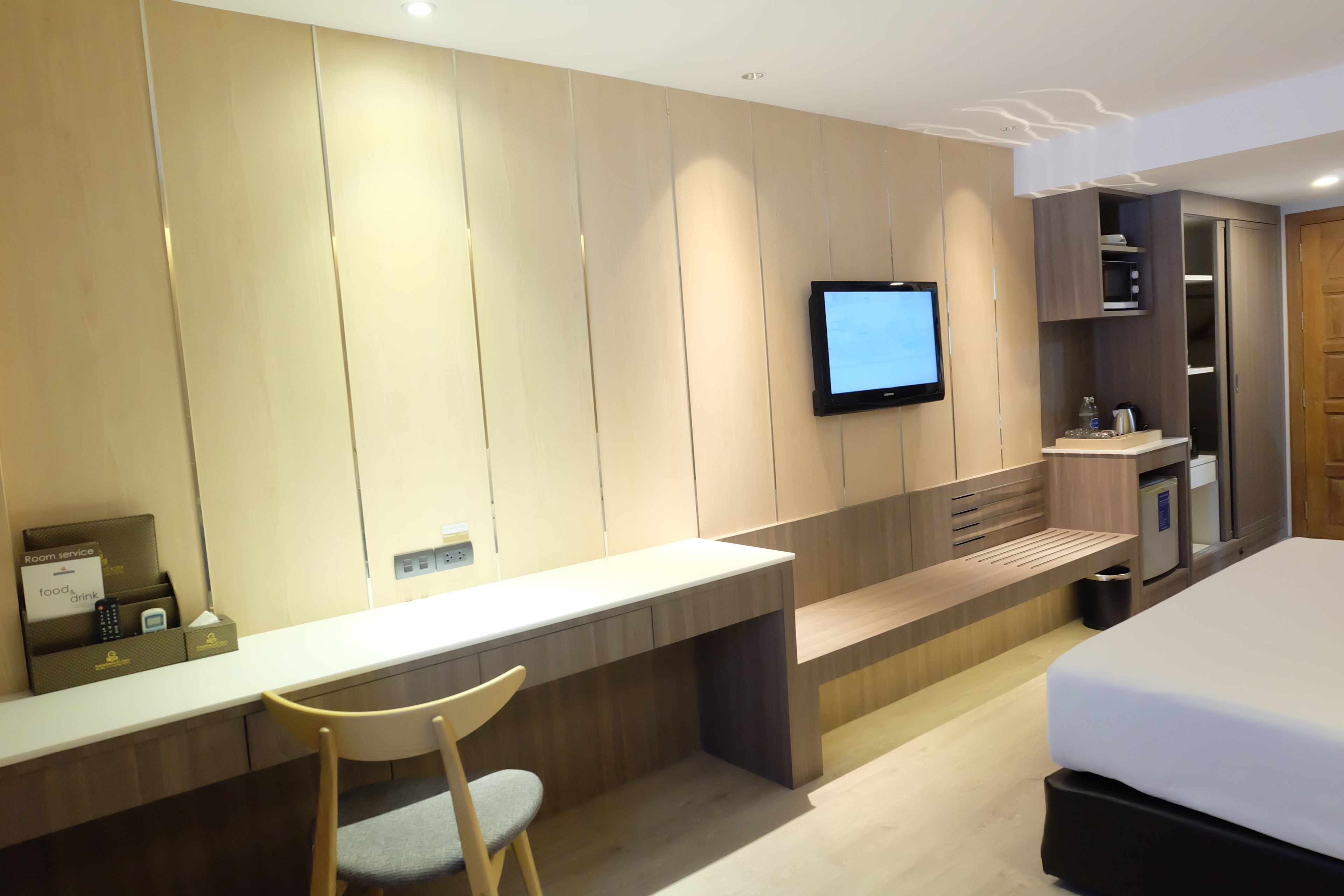Ein modernes Hotelzimmer mit Schreibtisch, Stuhl, Bett, Fernseher und integrierten Stauraum.