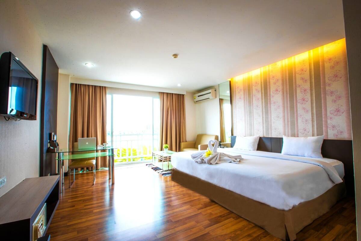 A hotel room with a bed, a desk, a television, and a balcony with a view.