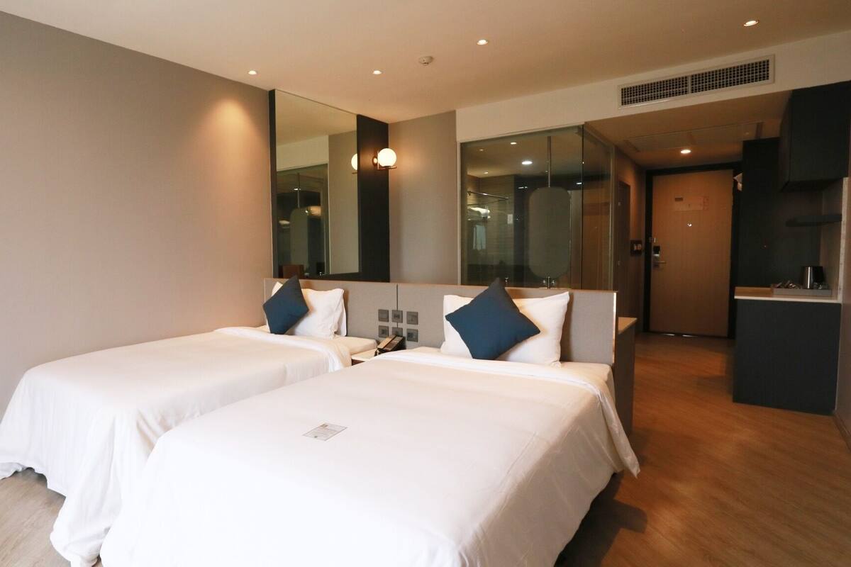 A hotel room with two beds, a large mirror, a small desk, and a kitchenette.
