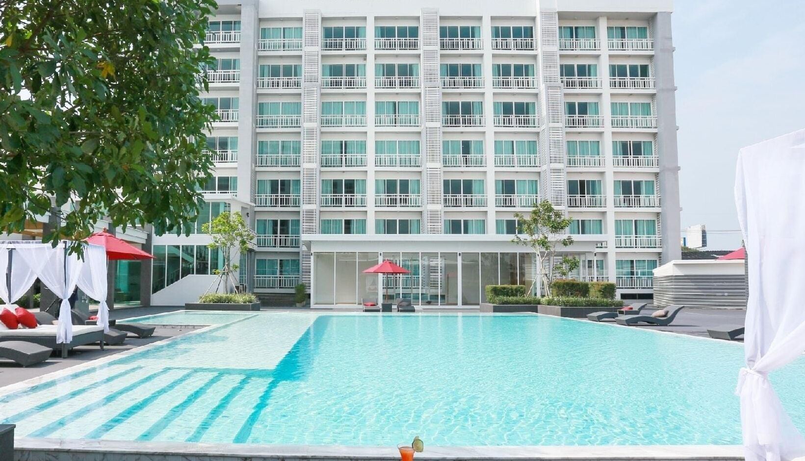 Un hotel con una piscina grande, varios balcones y zonas de estar al aire libre.