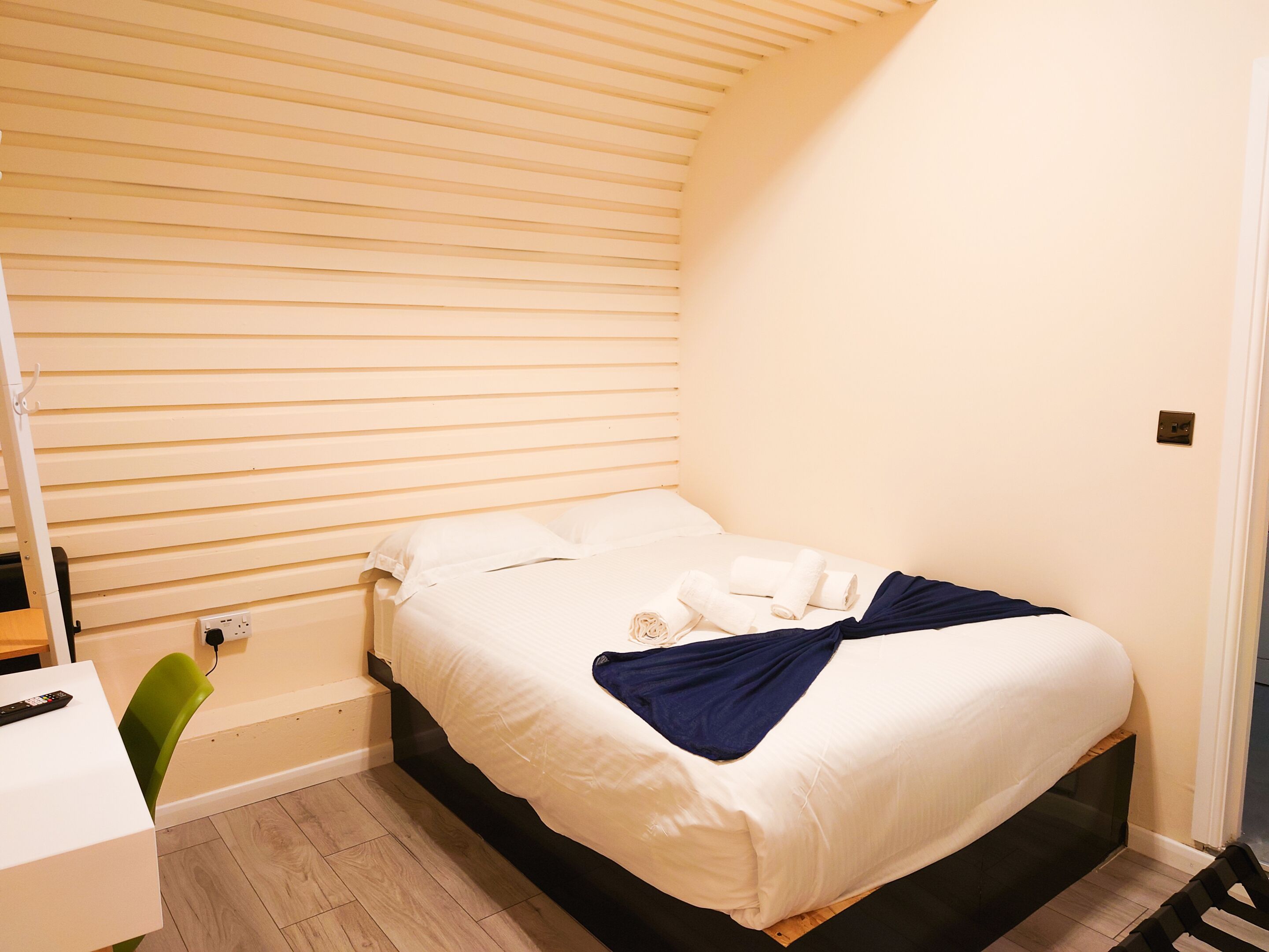 A small, neatly arranged bedroom with a single bed, a bedside table, and a chair.