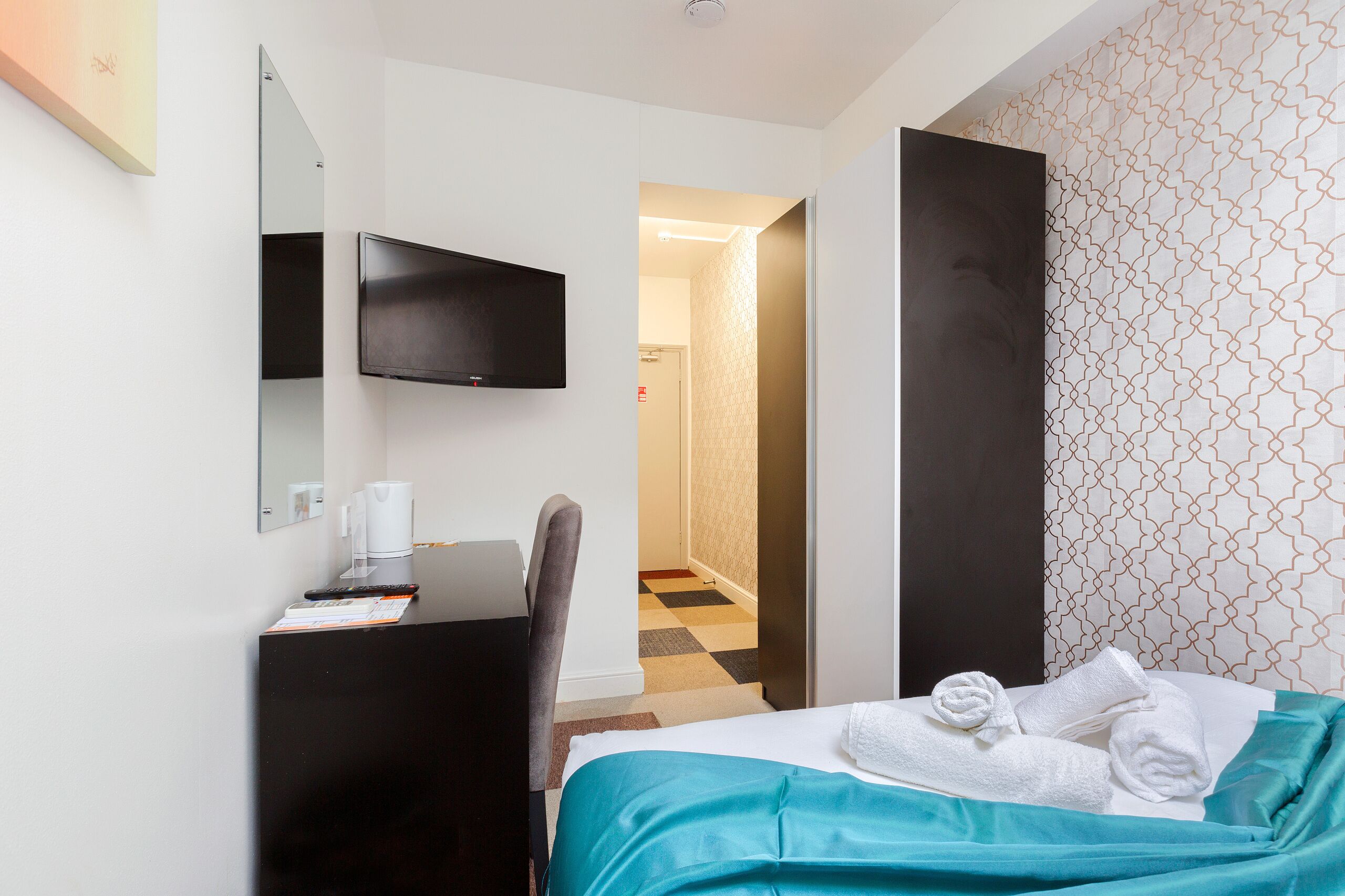 A hotel room with a bed, a desk, a chair, a TV, and a bathroom visible through an open door.