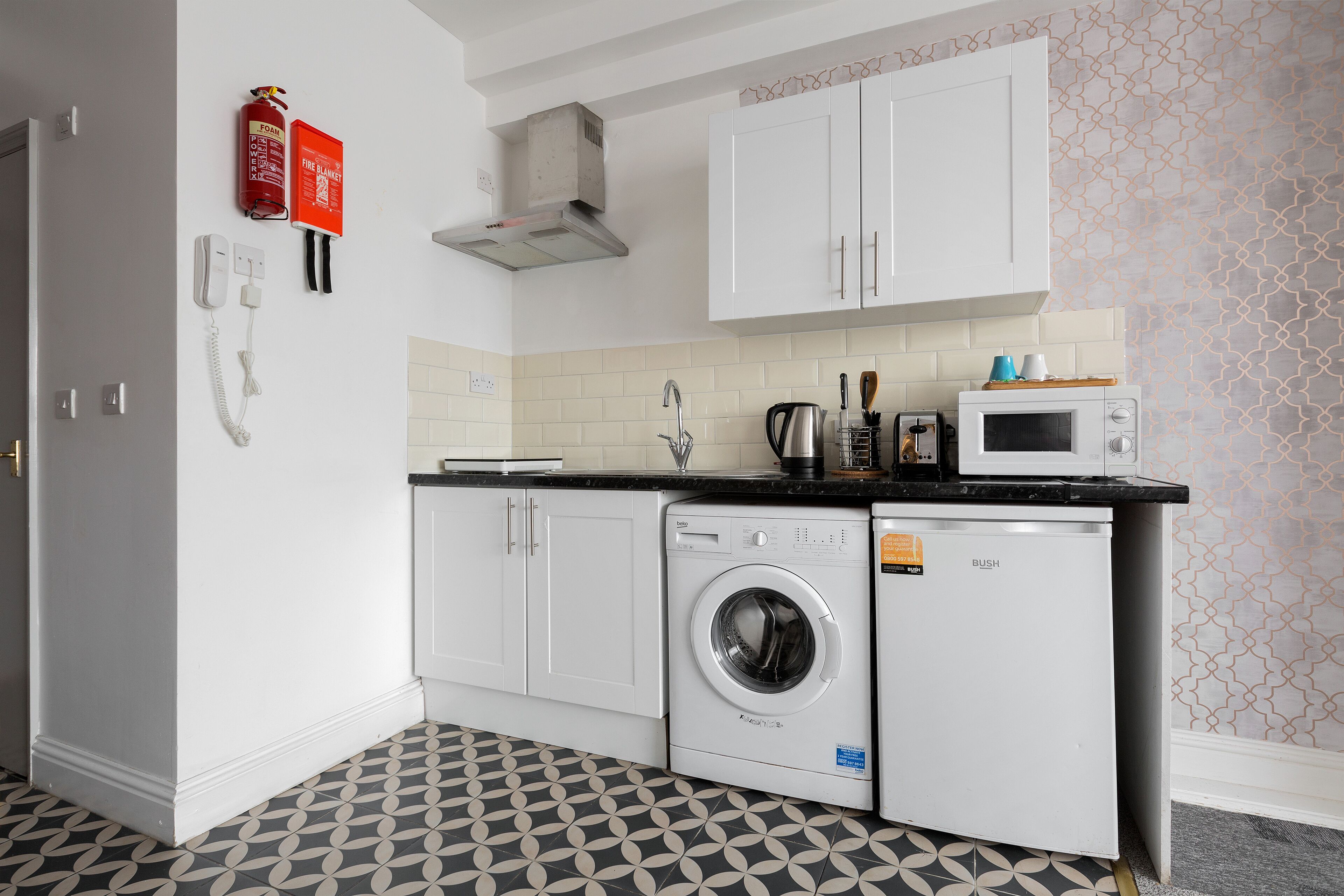 A compact kitchen with a washing machine, microwave, and a fire extinguisher.