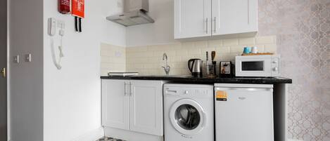 A compact kitchen with a washing machine, microwave, and a fire extinguisher.