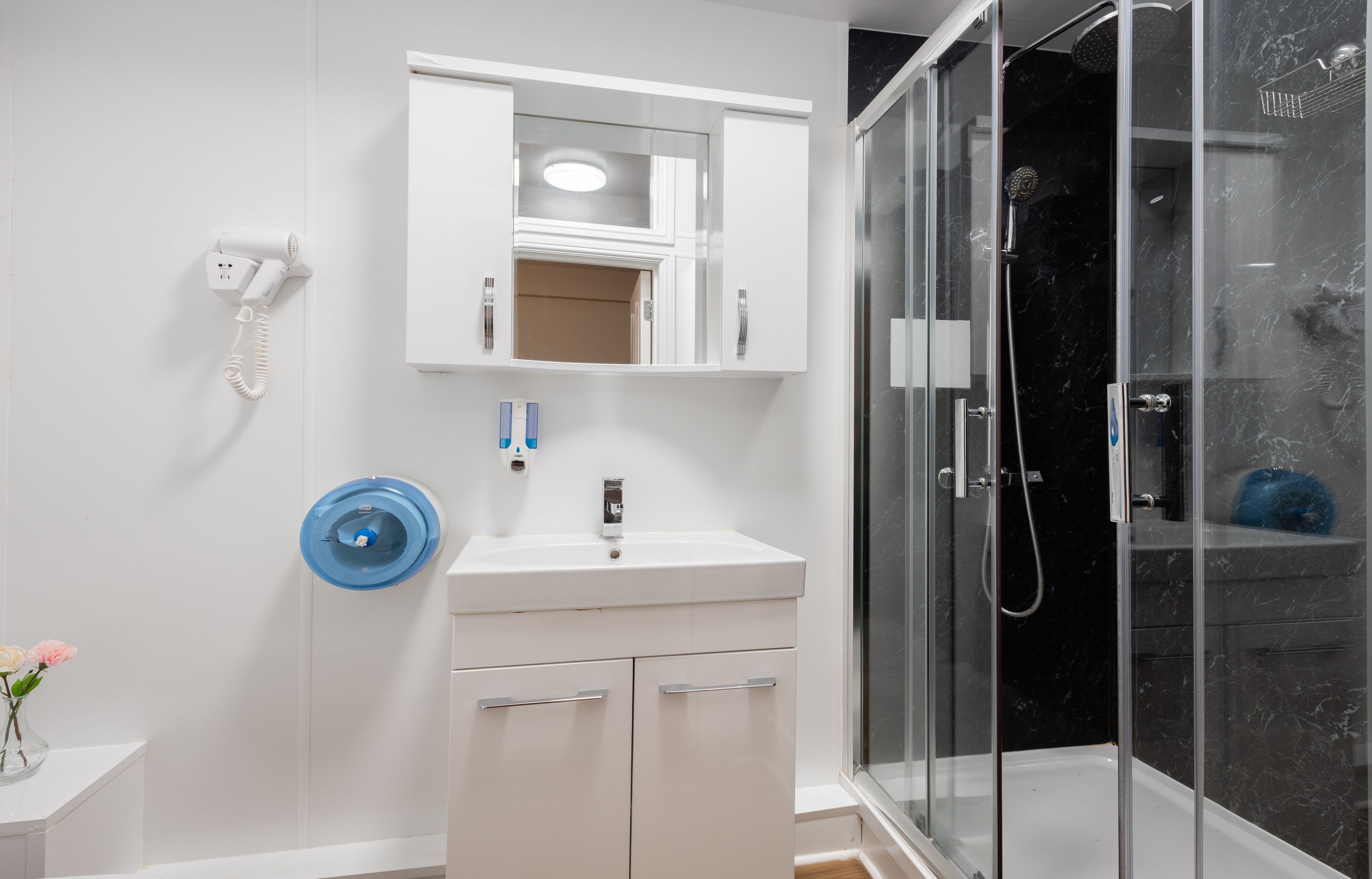 A modern bathroom with a glass shower enclosure, a white vanity with a sink, and a mounted phone.