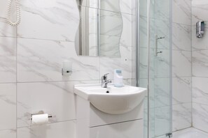 A modern bathroom with a glass shower enclosure, a white sink with a soap dispenser, and a toilet paper holder.