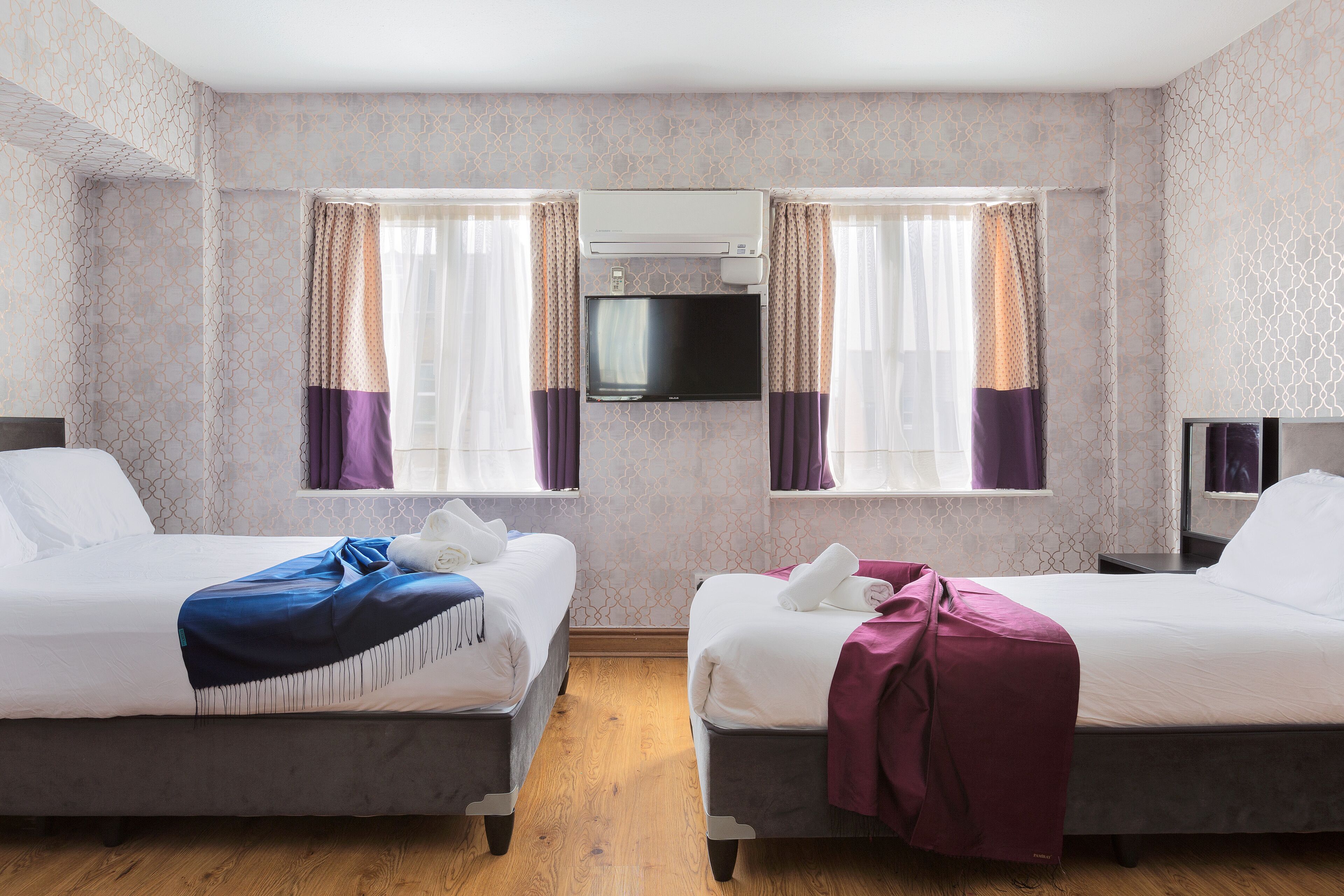 Una habitación de hotel con dos camas, un televisor montado en la pared y una ventana con cortinas.