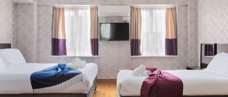 Una habitación de hotel con dos camas, un televisor montado en la pared y una ventana con cortinas.