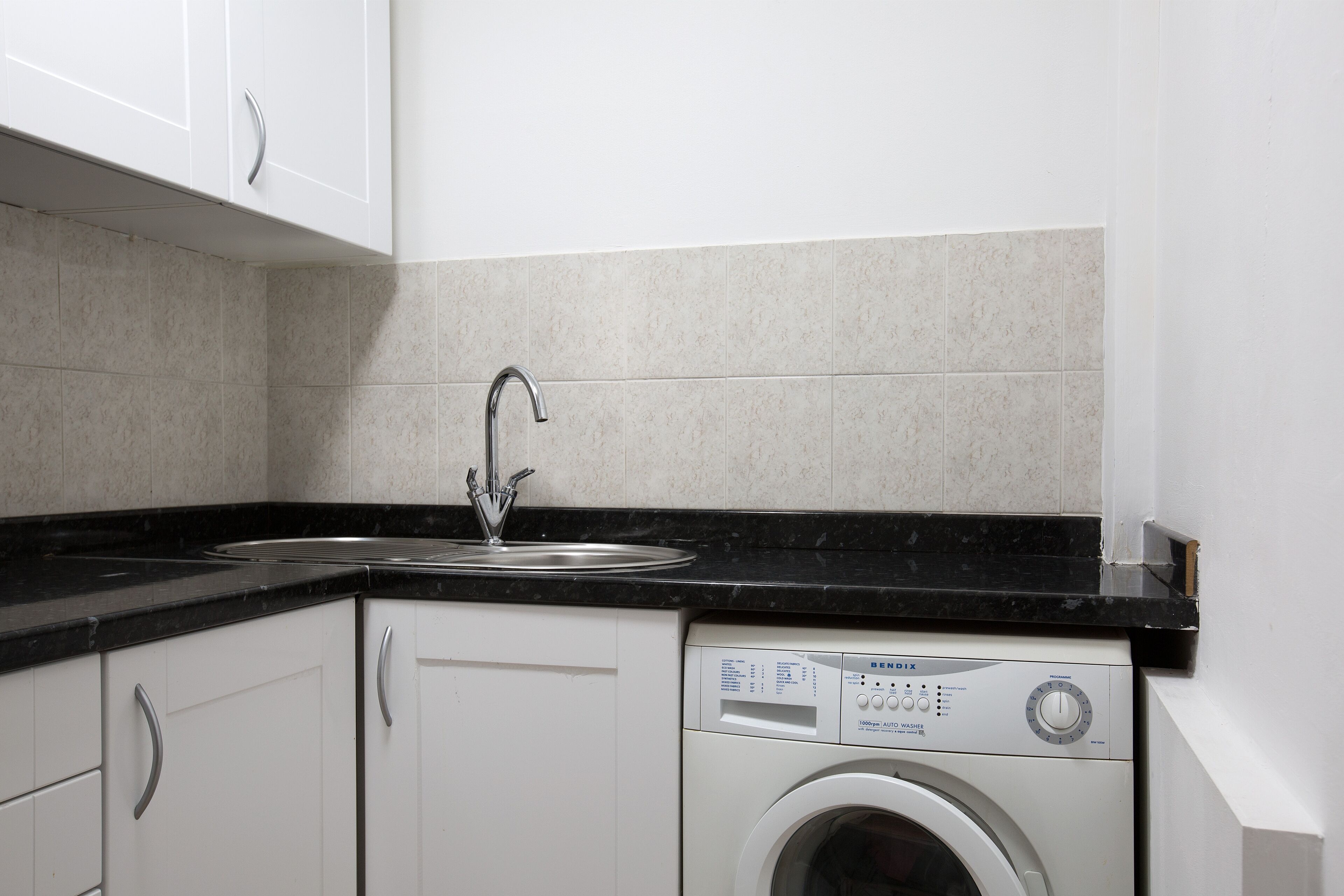 A kitchen with white cabinets, a black countertop, a stainless steel sink, and a front-loading washing machine.