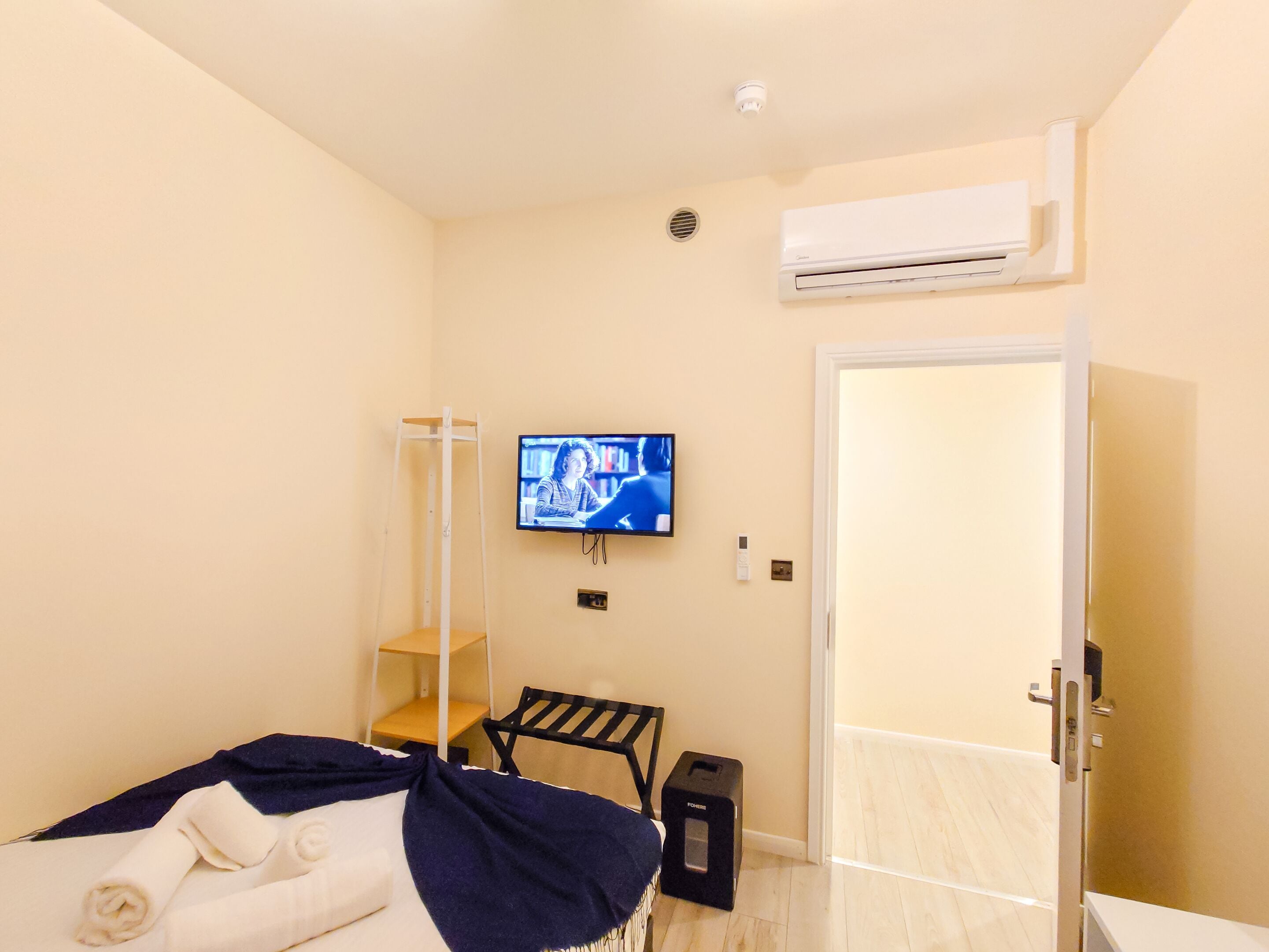 A hotel room with a bed, a TV mounted on the wall, a door, and a small table.