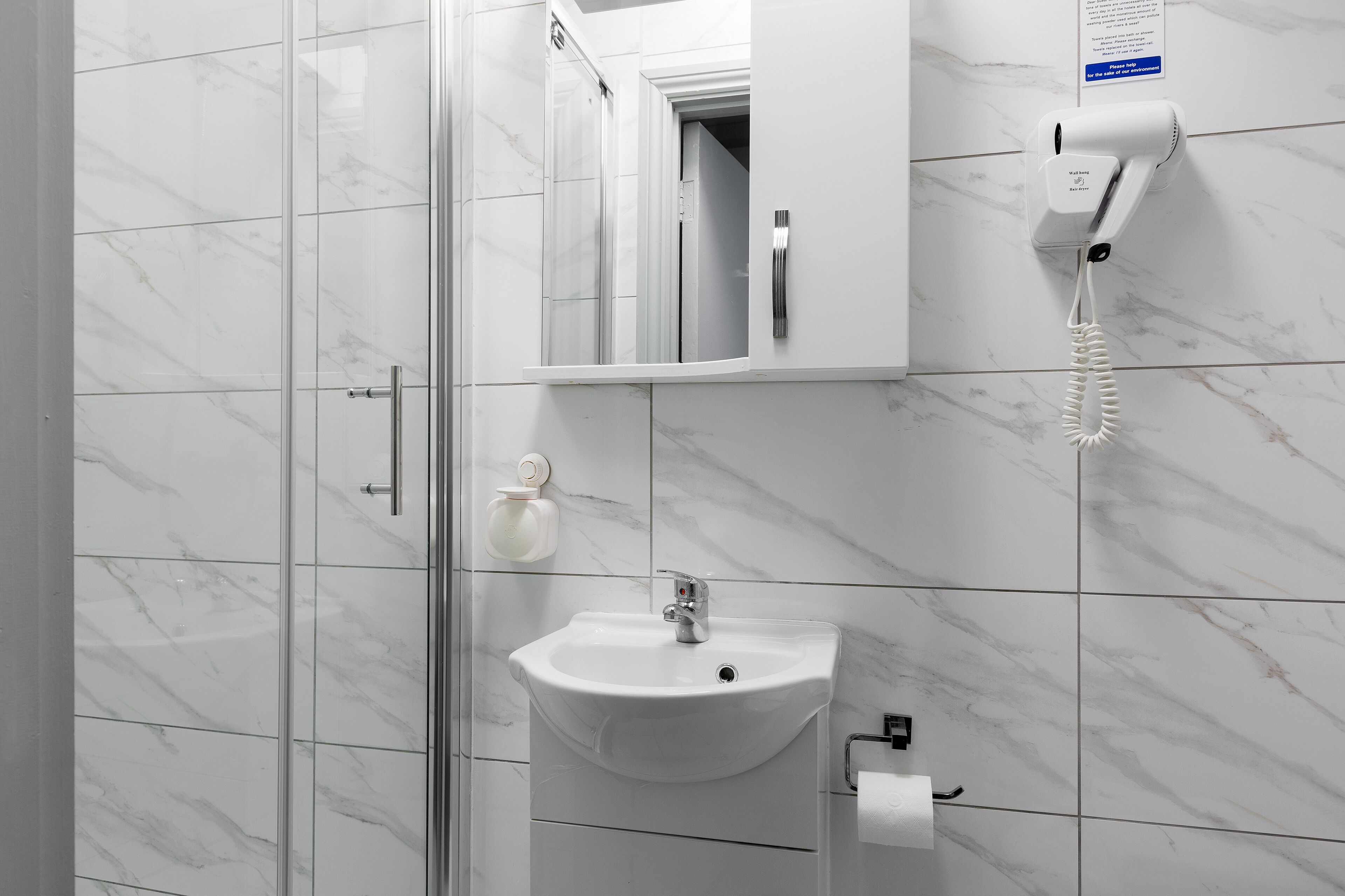 A modern bathroom with a glass shower enclosure, a white sink with a mirror above it, and a hairdryer mounted on the wall.