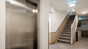 A modern elevator with a metallic finish, a staircase with patterned carpet, and a clean, minimalist interior design. - Central Hoxton Shoreditch (London)