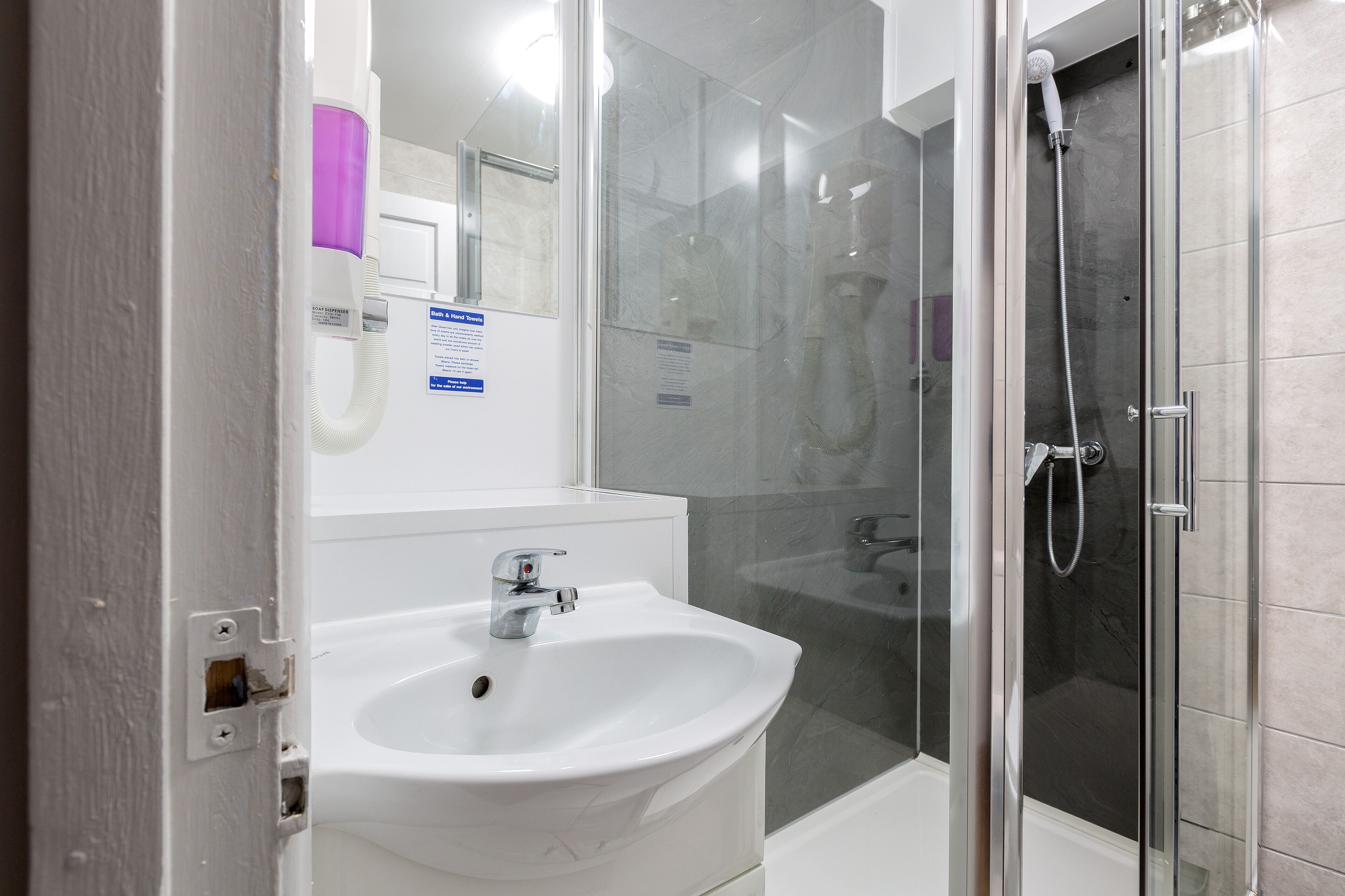 A modern bathroom with a white sink, a glass shower enclosure, and a visible hand dryer.