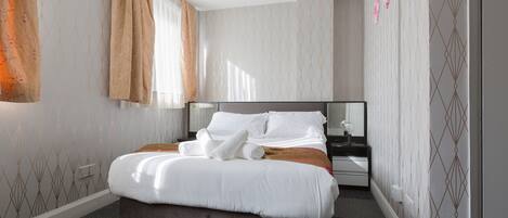 Moderni hotellihuone, jossa on suuri sänky, yöpöytä ja peili.