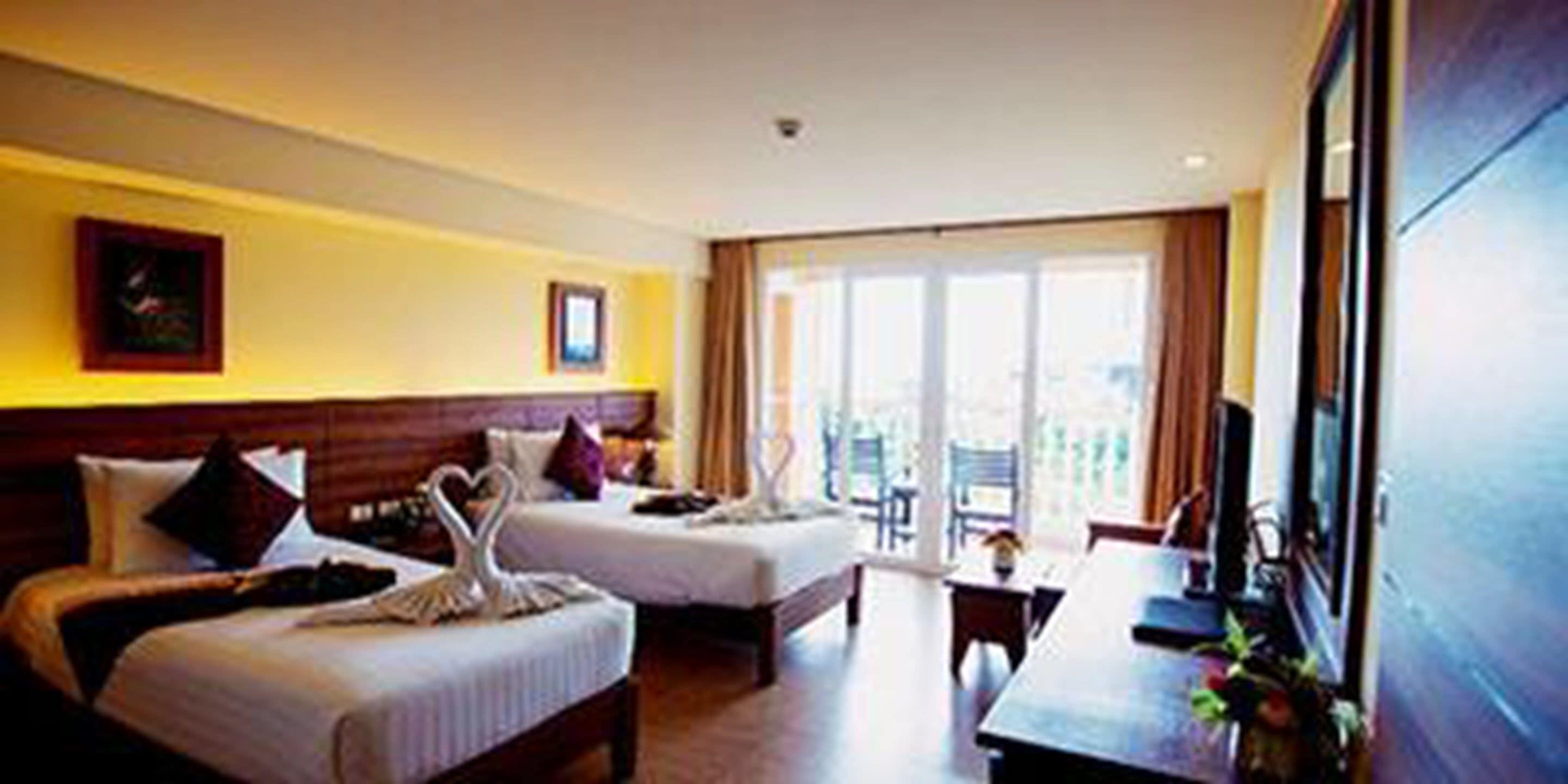 Habitación de hotel con dos camas, un escritorio y un balcón con vistas.
