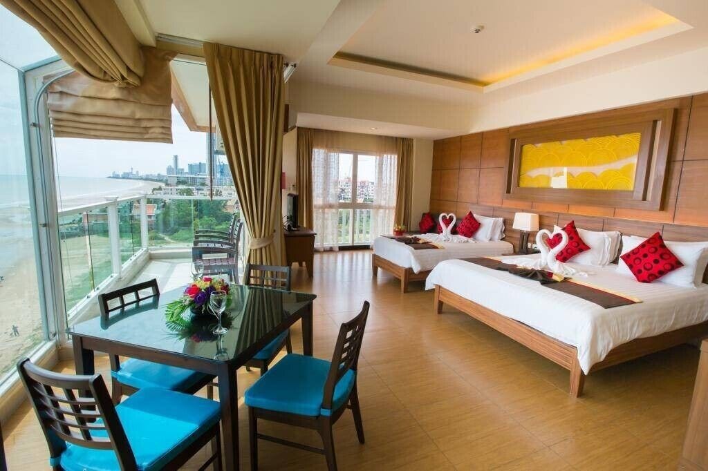 A hotel room with a balcony, two beds, a dining table, and a view of the city.