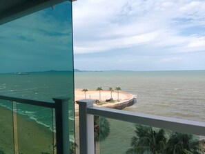 A view from a balcony overlooking a beach with palm trees and a distant ship. - Saisawan Beach Resort (Sattahip)