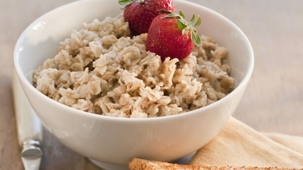 A bowl of oatmeal with strawberries on a wooden table, accompanied by a spoon and slices of bread on a napkin. - Element Hanover Lebanon (Lebanon)