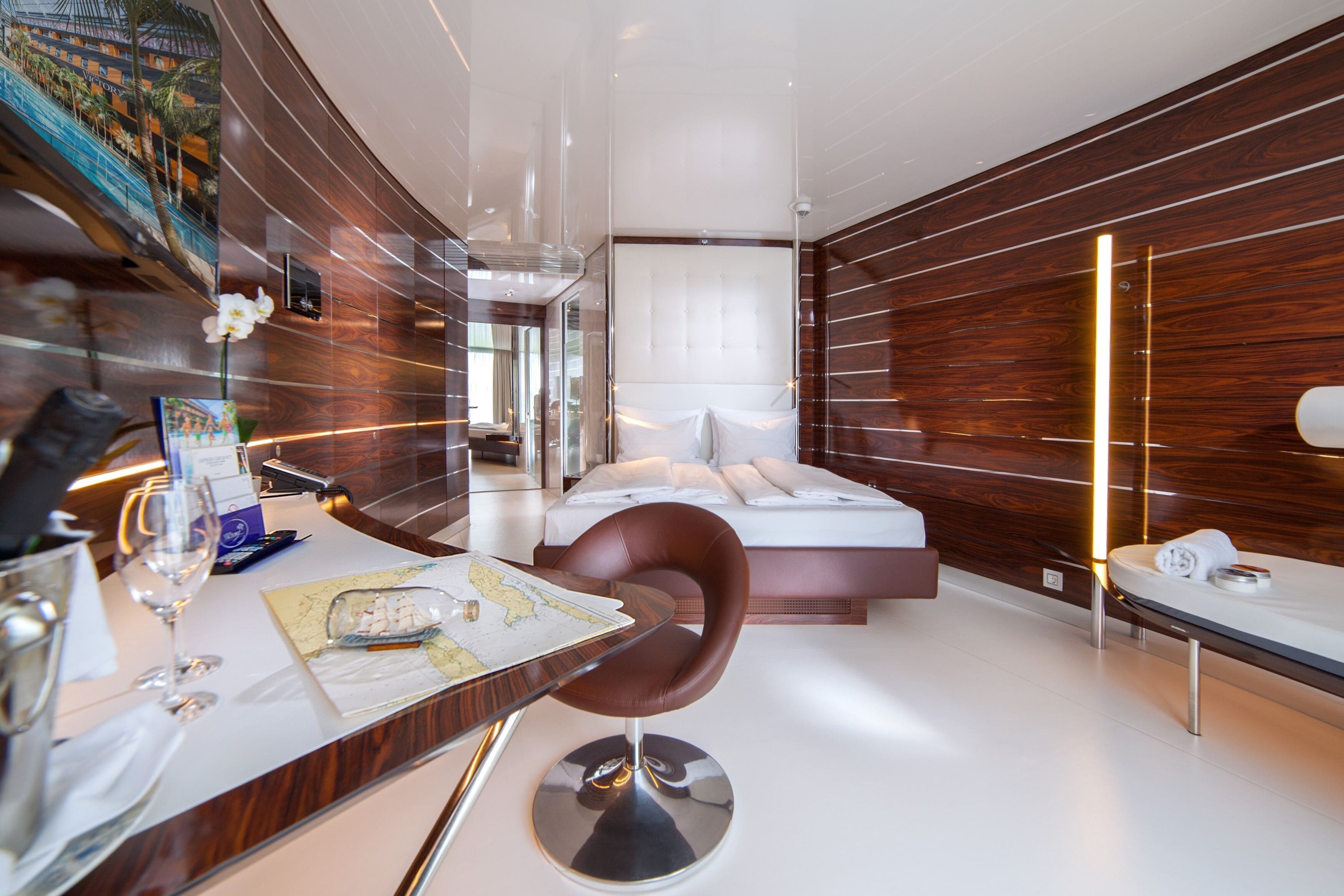 A modern hotel room with a large bed, a dining table with a map, a chair, and a minibar.