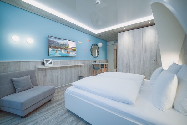 Quarto de hotel moderno com uma cama grande, um sofá, uma escrivaninha e uma TV fixada na parede.