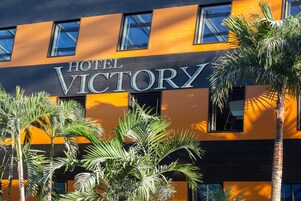 Un hotel llamado 'Hotel Victory' con una fachada moderna, ventanas grandes y palmeras en la entrada.